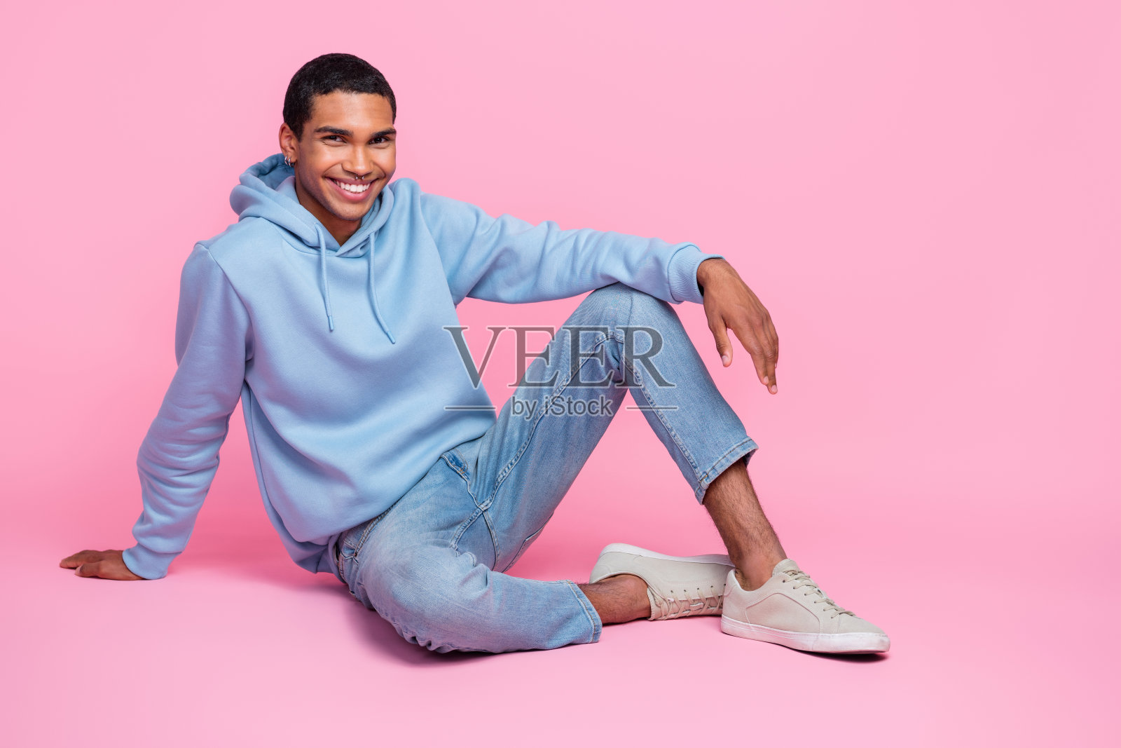 穿着漂亮服装的快乐男士坐在粉色背景下的空旷空间，宣传新款服装系列。照片摄影图片