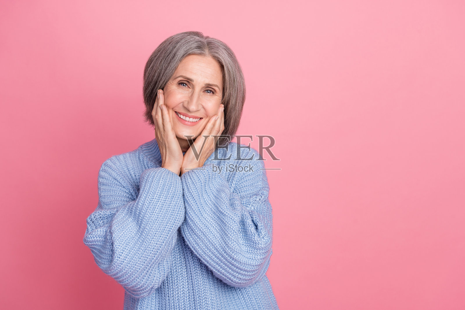 可爱的女士用手轻触脸颊，站在粉色背景的空旷空间中，宣传护肤产品。照片摄影图片