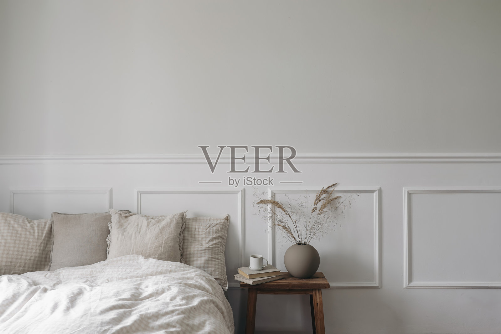 优雅的波西米亚风格卧室内饰。复古木质床头柜。现代圆形花瓶内插干草。旧书上的咖啡杯。米色格子床上用品。白色墙壁背景。斯堪的纳维亚风格家居，无人。照片摄影图片