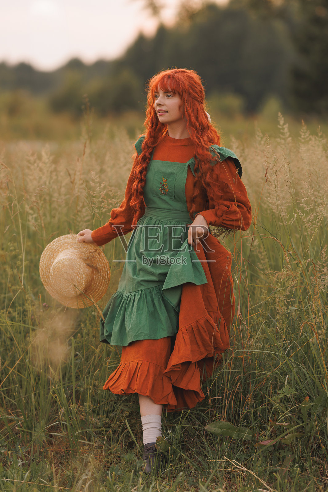 一位红发绿裙的女牧羊人在花海中坐着。照片摄影图片