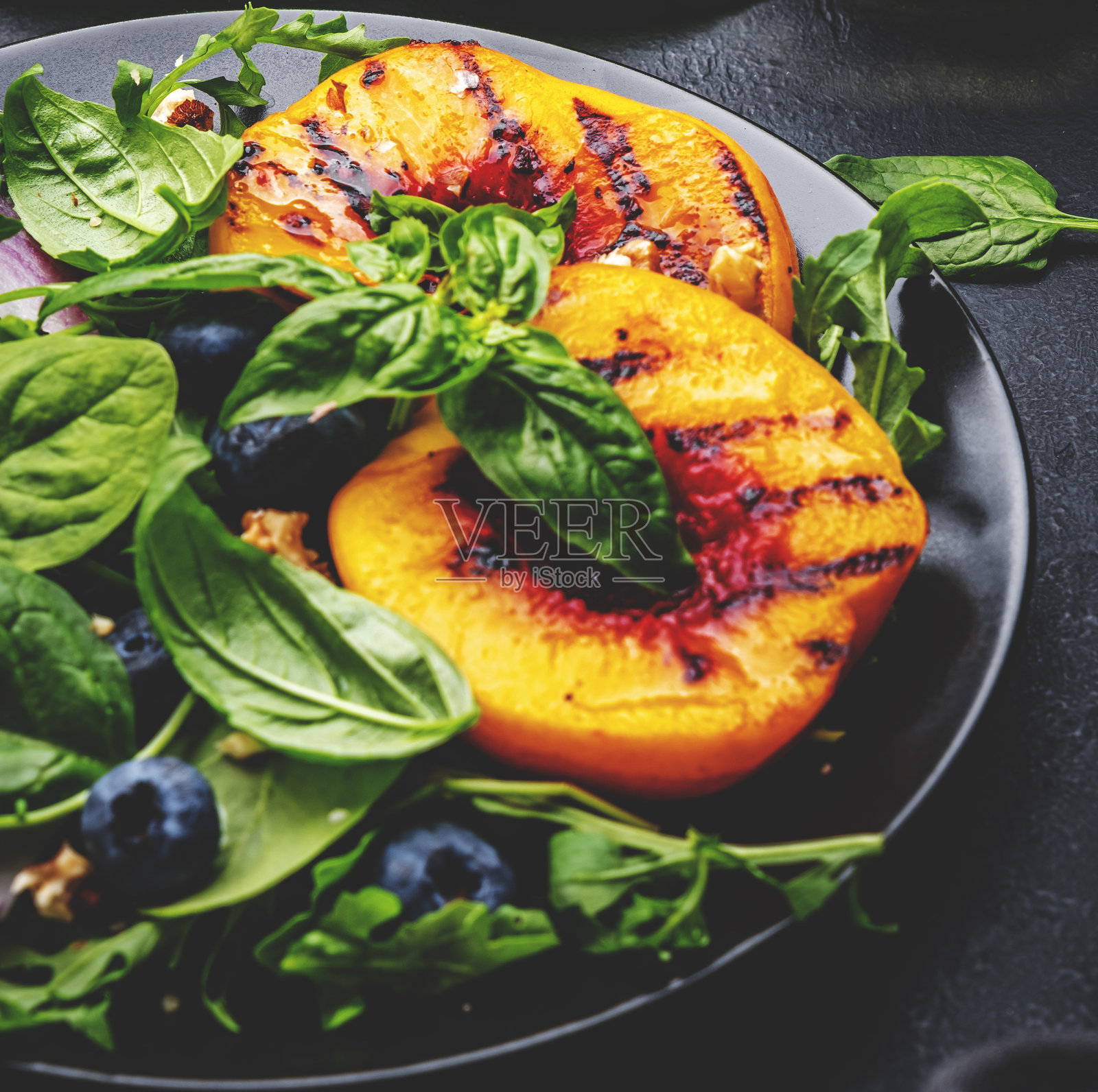 美味的素食沙拉，配有烤桃子、新鲜蓝莓、红洋葱、核桃、罗勒和混合香草，黑色背景，俯视图照片摄影图片