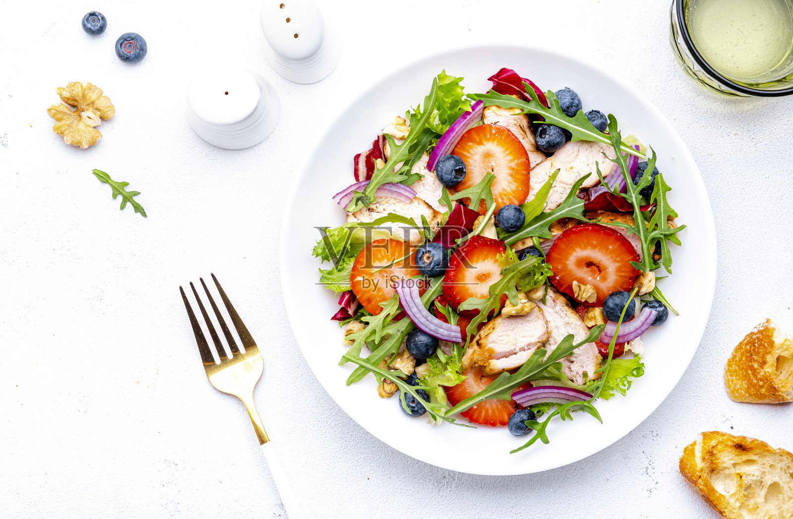 草莓鸡肉新鲜沙拉，配有芝麻菜、蓝莓、洋葱和核桃，白色背景，俯视图照片摄影图片