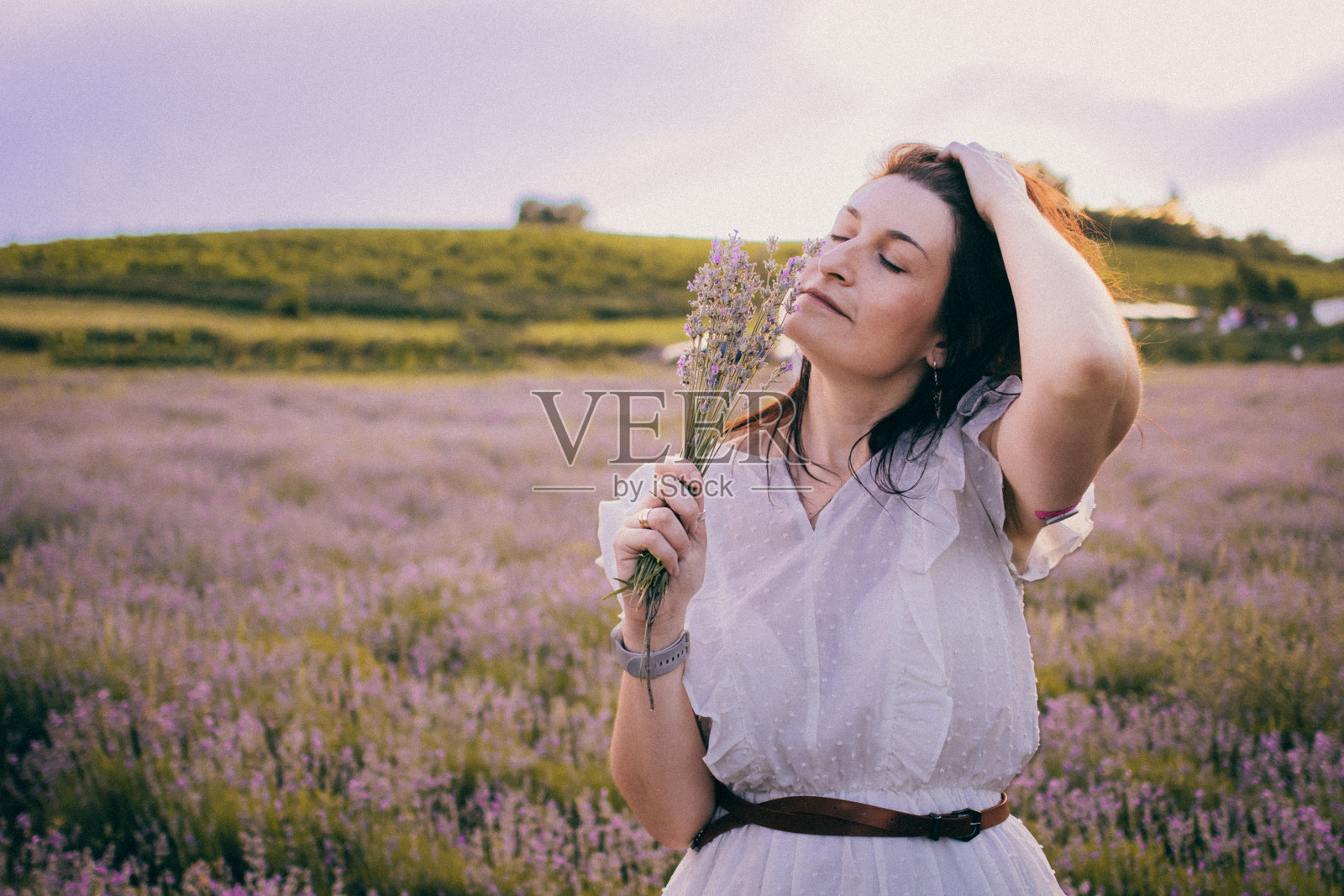 穿着白色连衣裙和草帽的女人在薰衣草田中享受快乐时光。对于糖尿病患者来说，这是一段幸福和快乐的时刻。她的上臂后部佩戴着小型传感器以监测血糖。照片摄影图片
