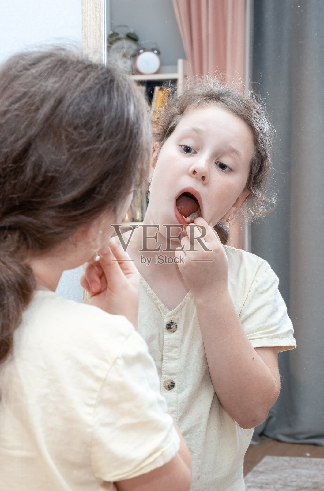 一个9岁的女孩牙疼，一名白人儿童在镜子前检查她的疼痛牙齿。照片摄影图片