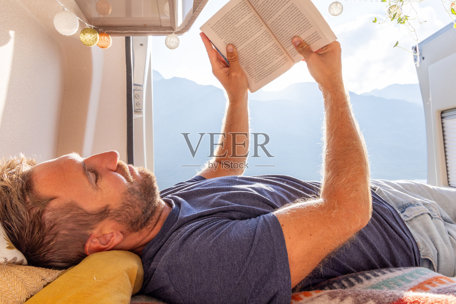 男子躺在房车里阅读书籍，享受山景照片摄影图片
