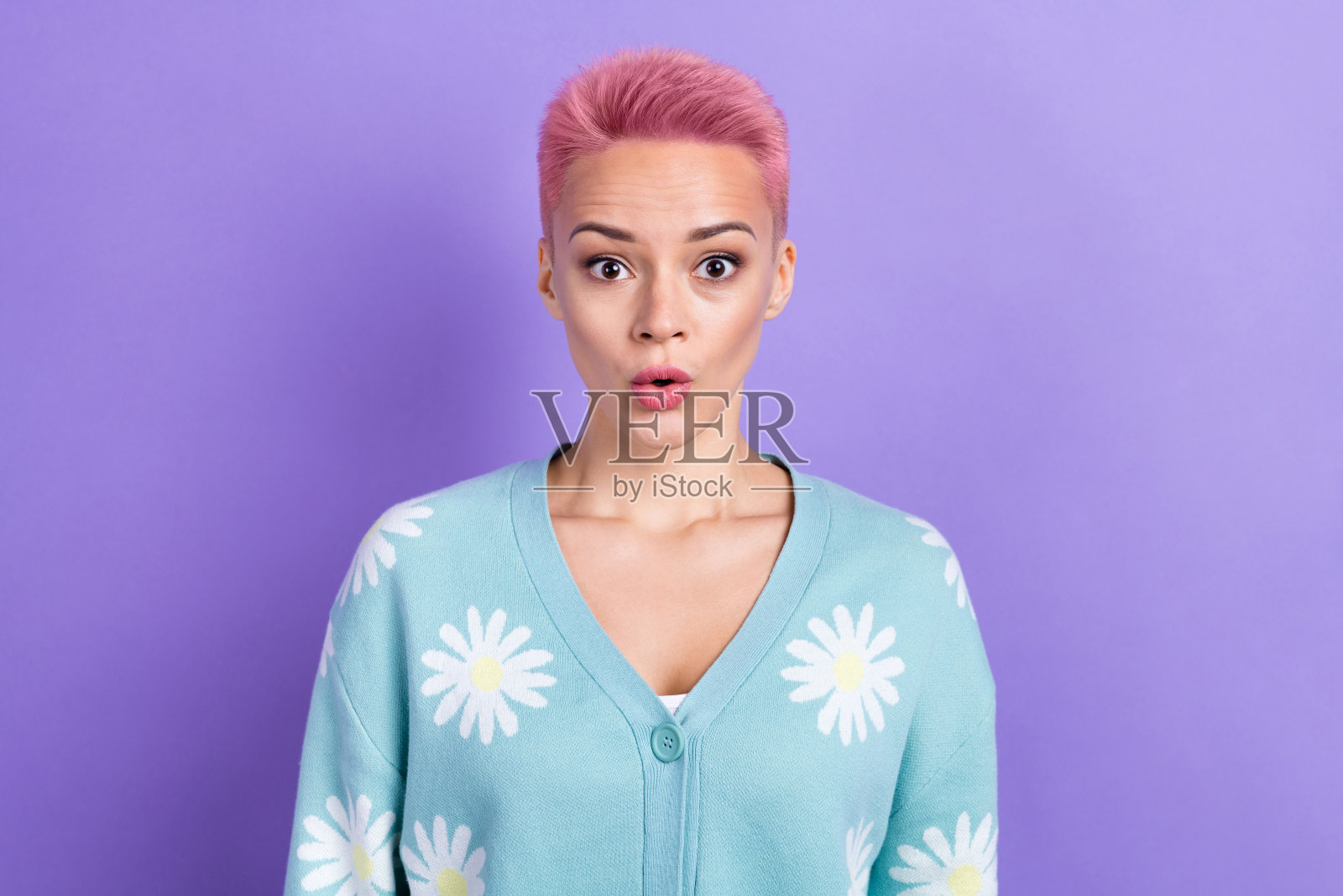 一位积极、愉快、惊讶的女孩，粉色发型，穿着蓝色毛衣，张嘴凝视，背景为紫色。照片摄影图片