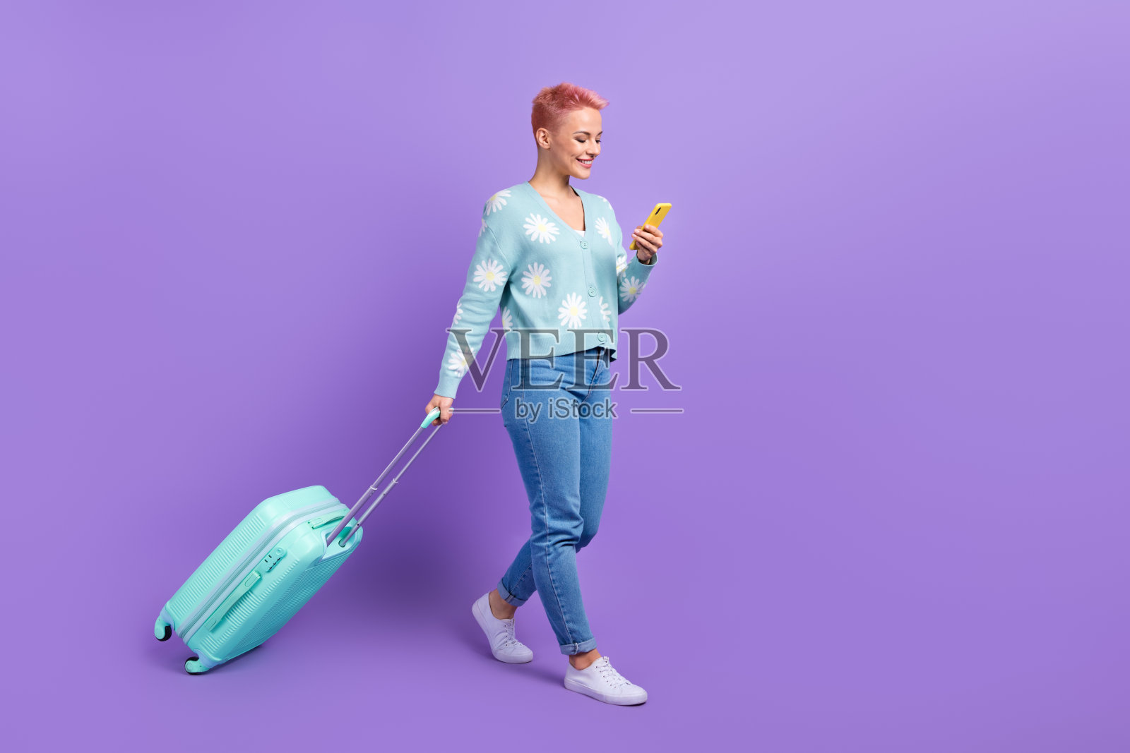 全身照的积极博主女性在机场走动，手提行李，订购低成本航班的广告，背景为紫色。照片摄影图片