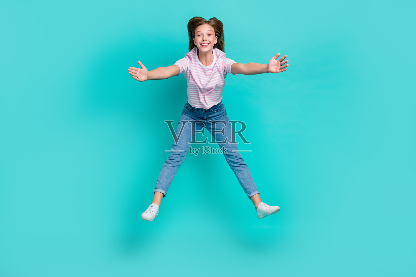 穿着条纹T恤的时尚女士在空旷的空间中跳跃，双臂张开，背景为青绿色。照片摄影图片