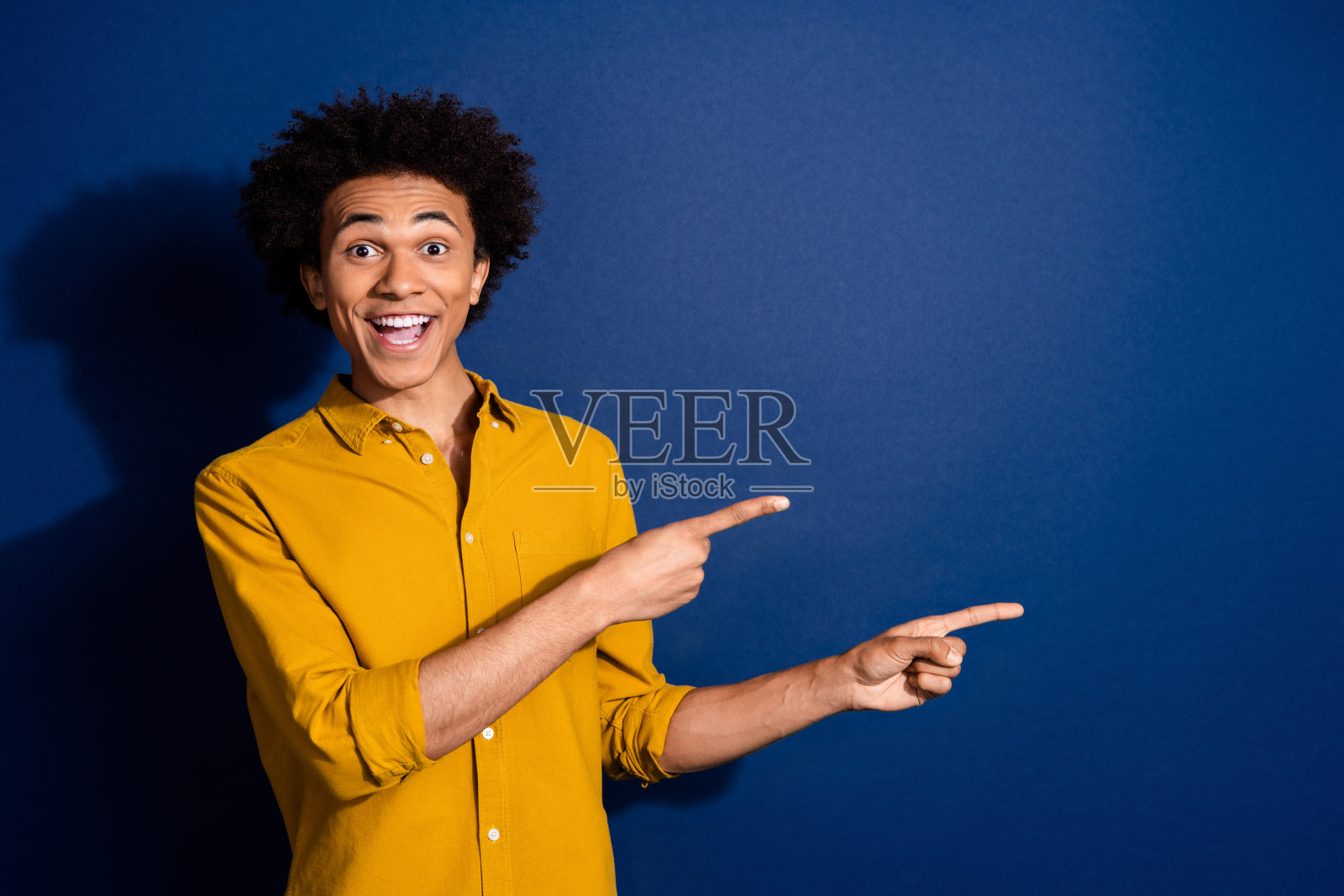 年轻男子的肖像，手指指向空白处，穿着黄色衬衫，背景为深蓝色。照片摄影图片