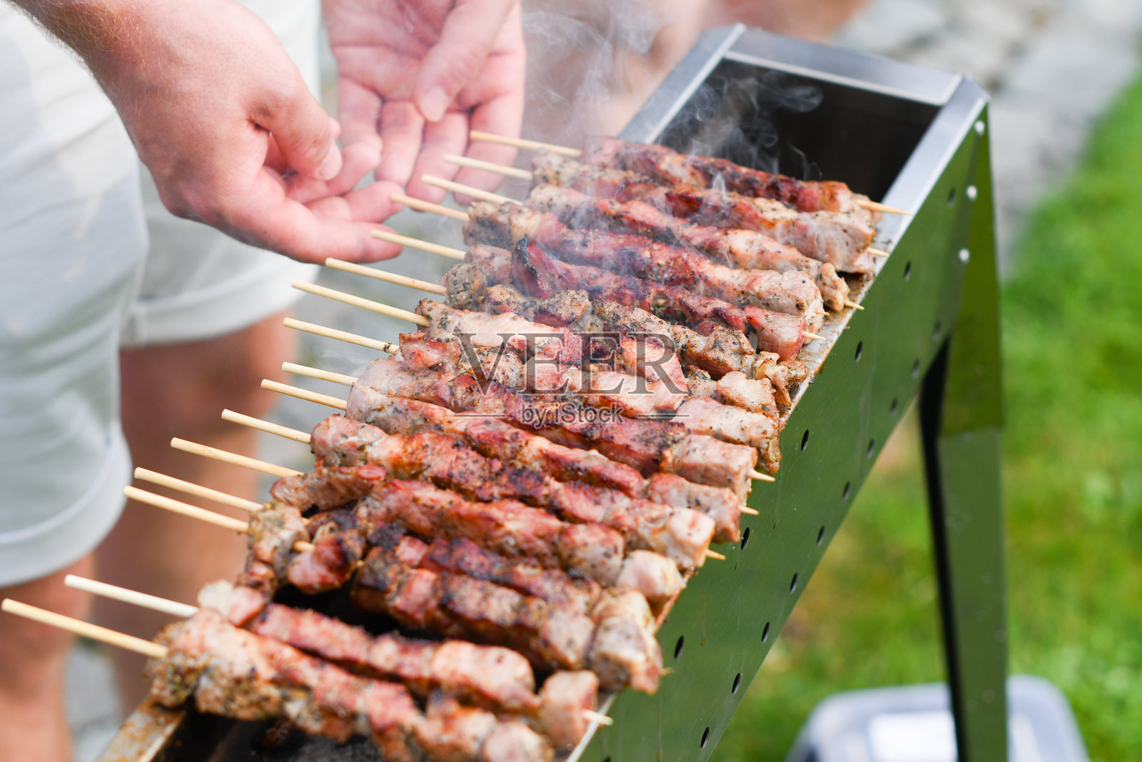 年轻男子在炭火上烤肉串，阿罗斯蒂奇尼 - 典型的意大利南部美食，奢华的阳台野餐照片摄影图片