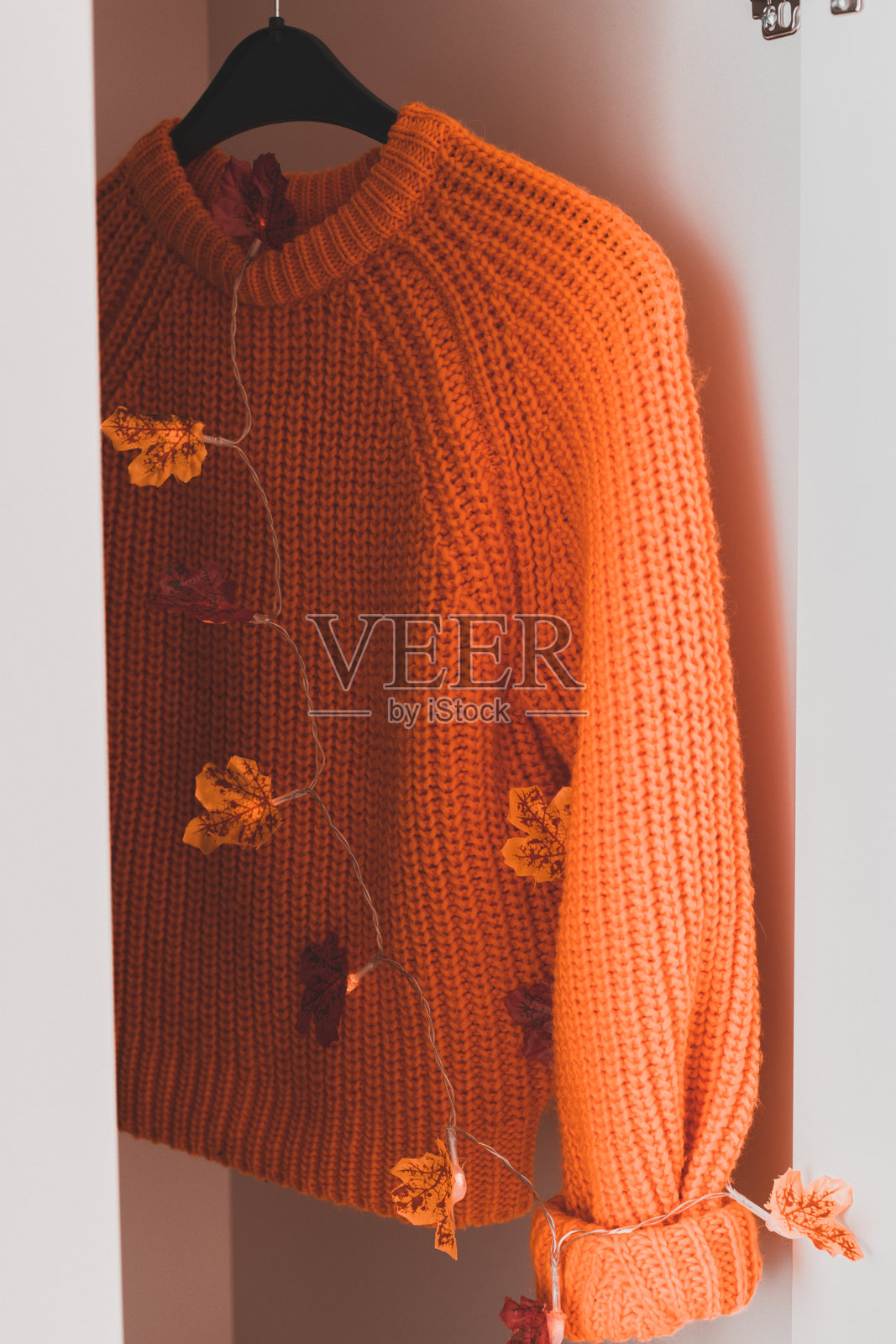 衣柜里挂着一件橙色毛衣。照片摄影图片