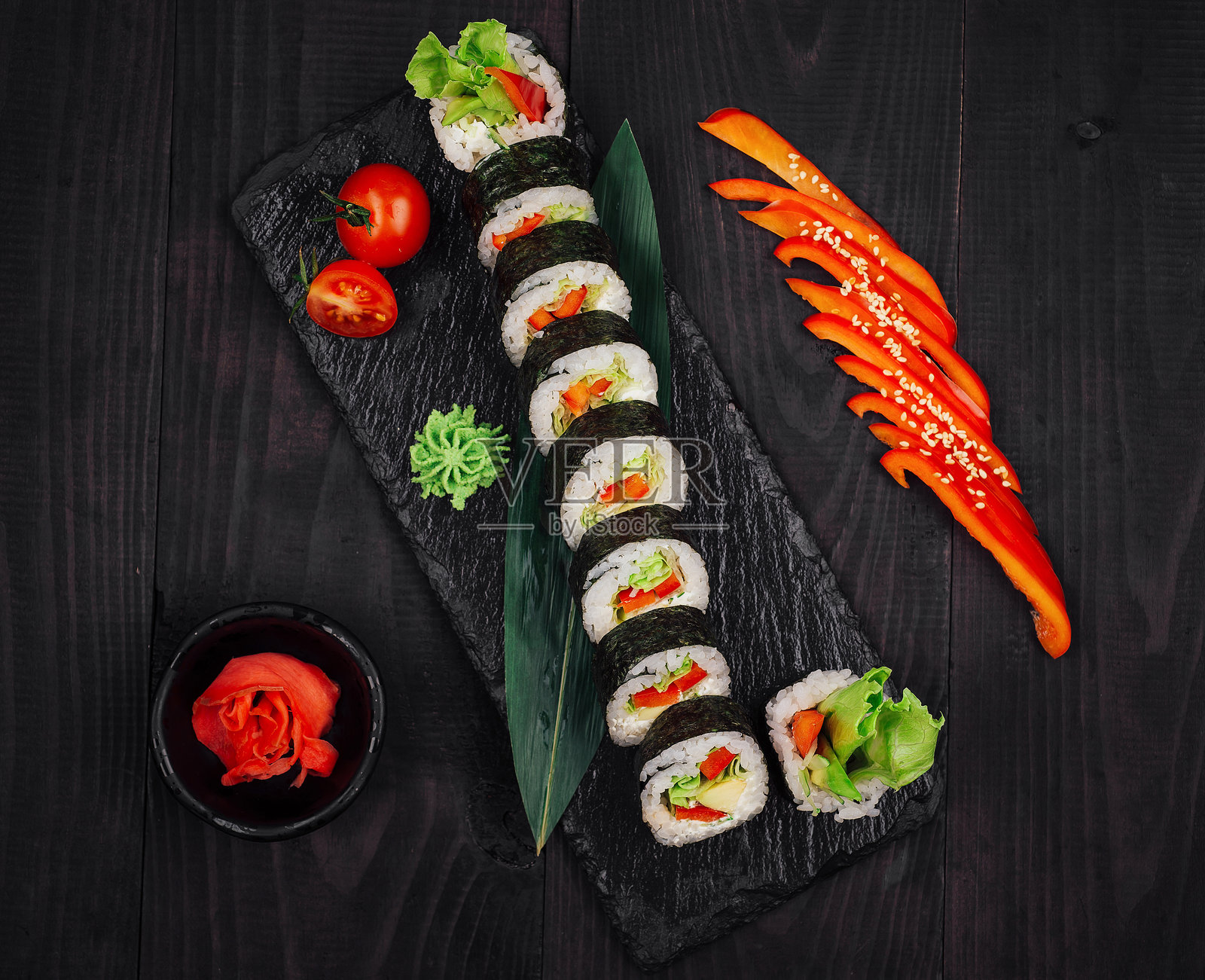 寿司卷摆放在黑色石板托盘上，旁边有红椒和芥末照片摄影图片