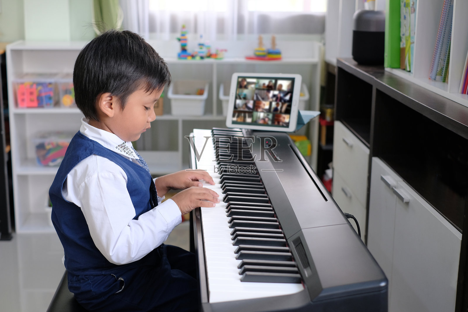 五岁小孩学习音乐课程的肖像。快乐的亚洲小男孩在家里用平板电脑在线学习钢琴。照片摄影图片