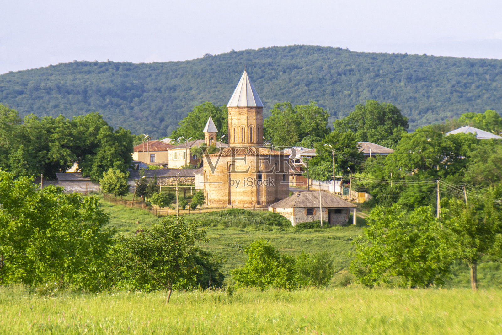 绿色草地上的田野，森林边缘，科达洛村的砖砌教堂。背景是山脉和湛蓝的天空。照片摄影图片