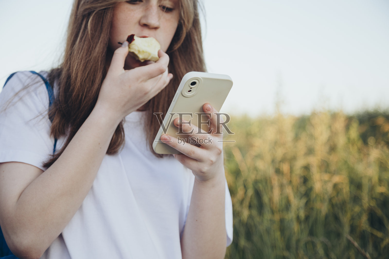 在户外吃苹果并使用手机的少女，留白空间。照片摄影图片
