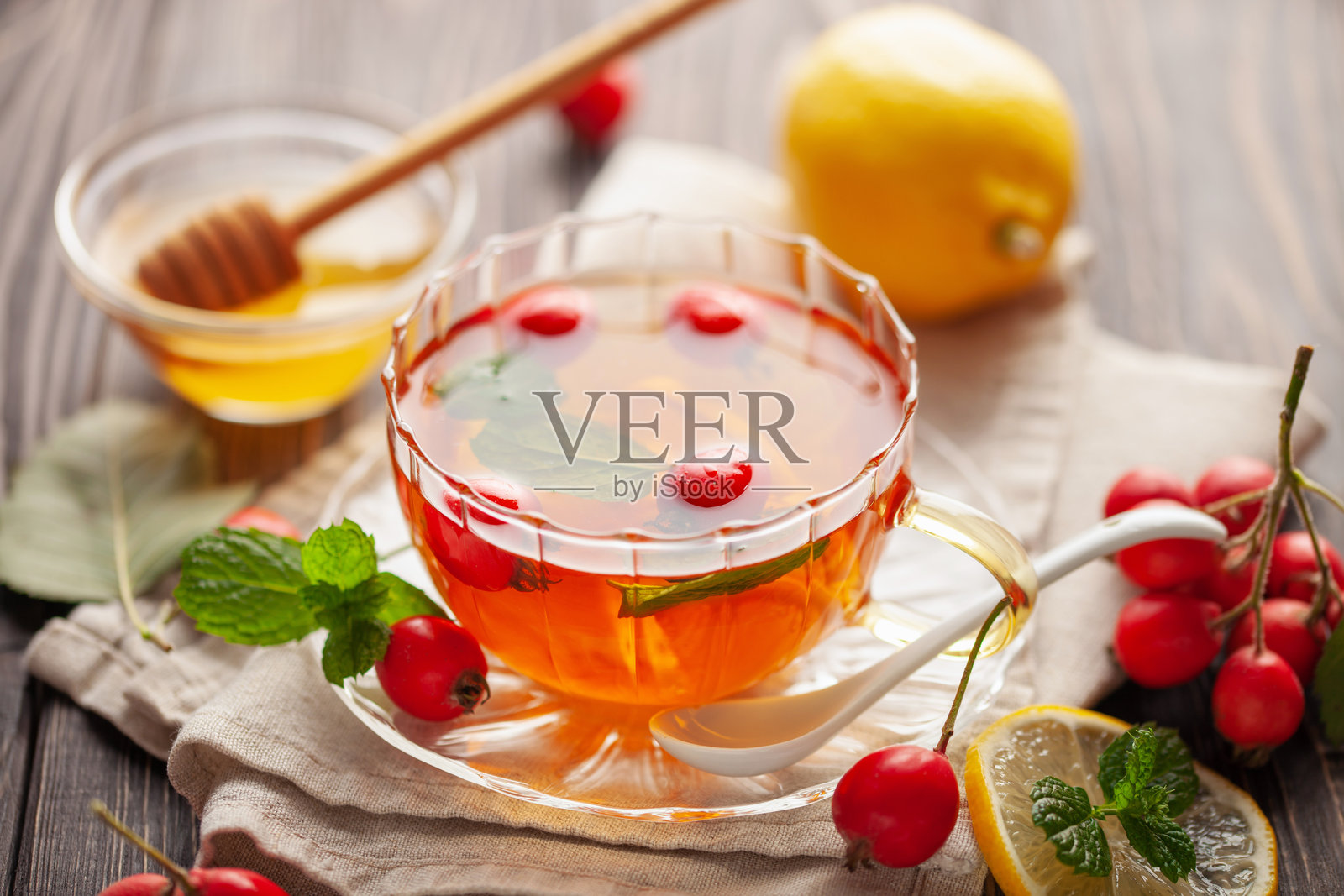 桌子上放着一杯盛有山楂茶、薄荷叶、蜂蜜和柠檬的玻璃杯。维生素健康饮品。照片摄影图片