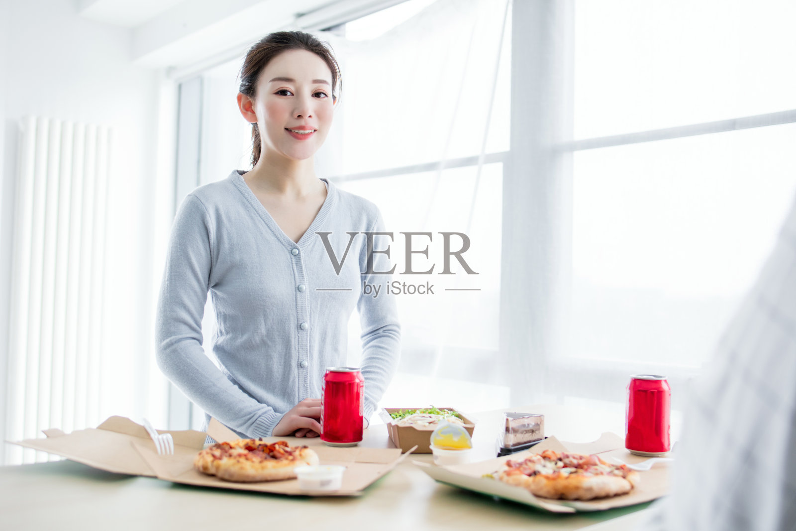 快乐的年轻女性朋友们在家里的沙发上吃披萨，喝葡萄酒。快乐微笑的年轻女性朋友们在家里吃披萨并打开一瓶葡萄酒。照片摄影图片