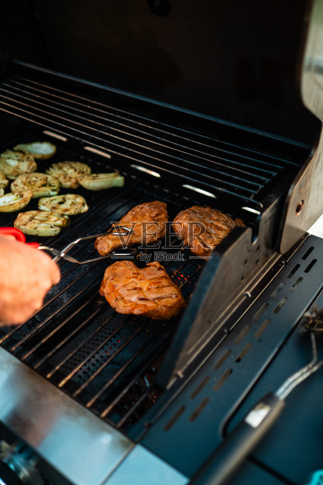 一个人在阳光明媚的夏季日子里，使用大型家用燃气烤架烤制牛排和蔬菜，火焰熊熊。照片摄影图片