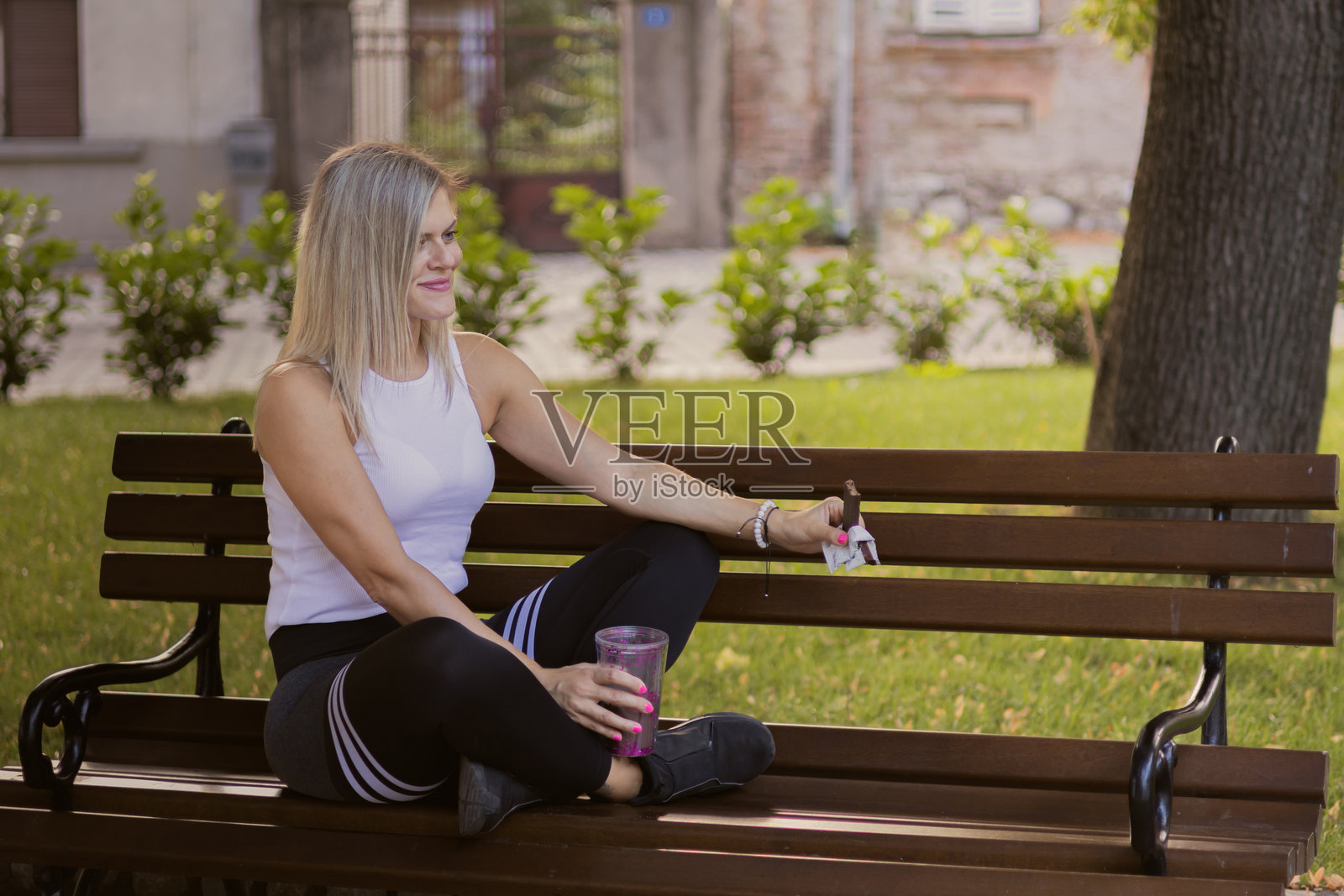 美丽的金发健身女性在公共公园户外训练后吃蛋白质棒和喝蛋白质奶昔。照片摄影图片