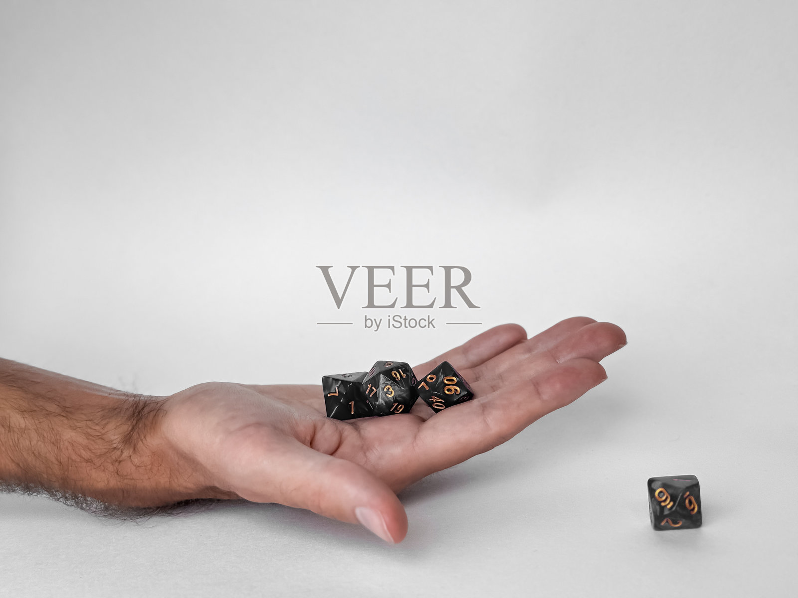 手握黑色多面骰子，背景为浅色。照片摄影图片