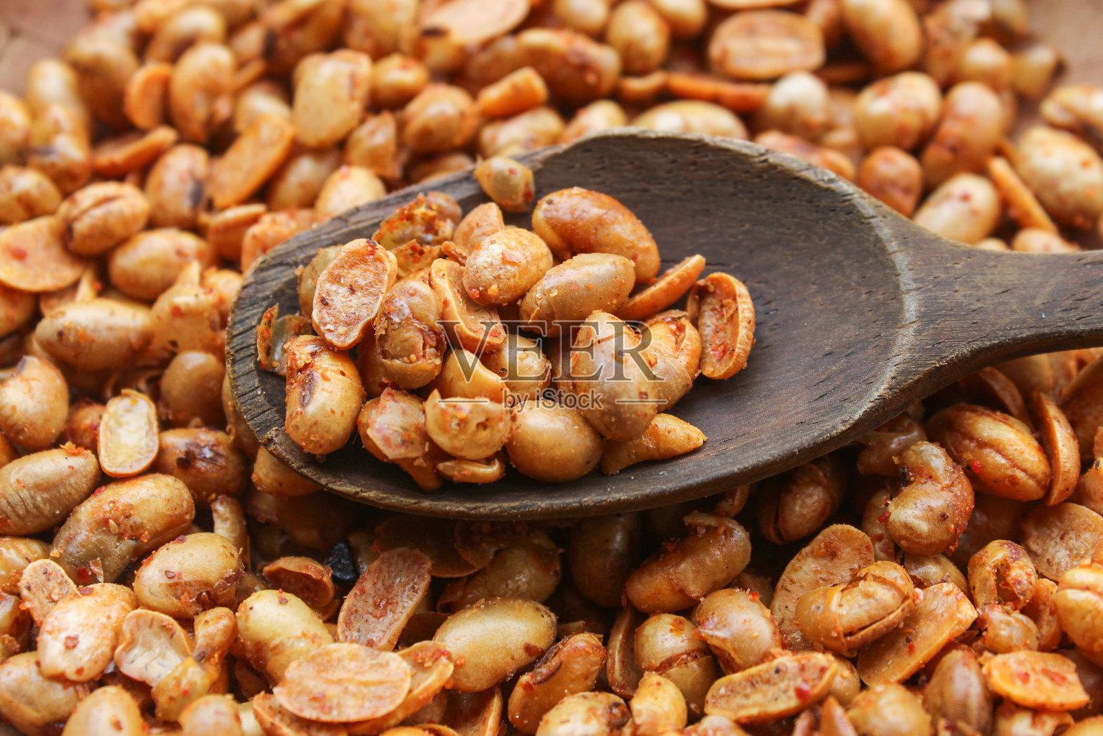 特写镜头：木勺上的调味花生，背景是一堆花生。花生零食。照片摄影图片
