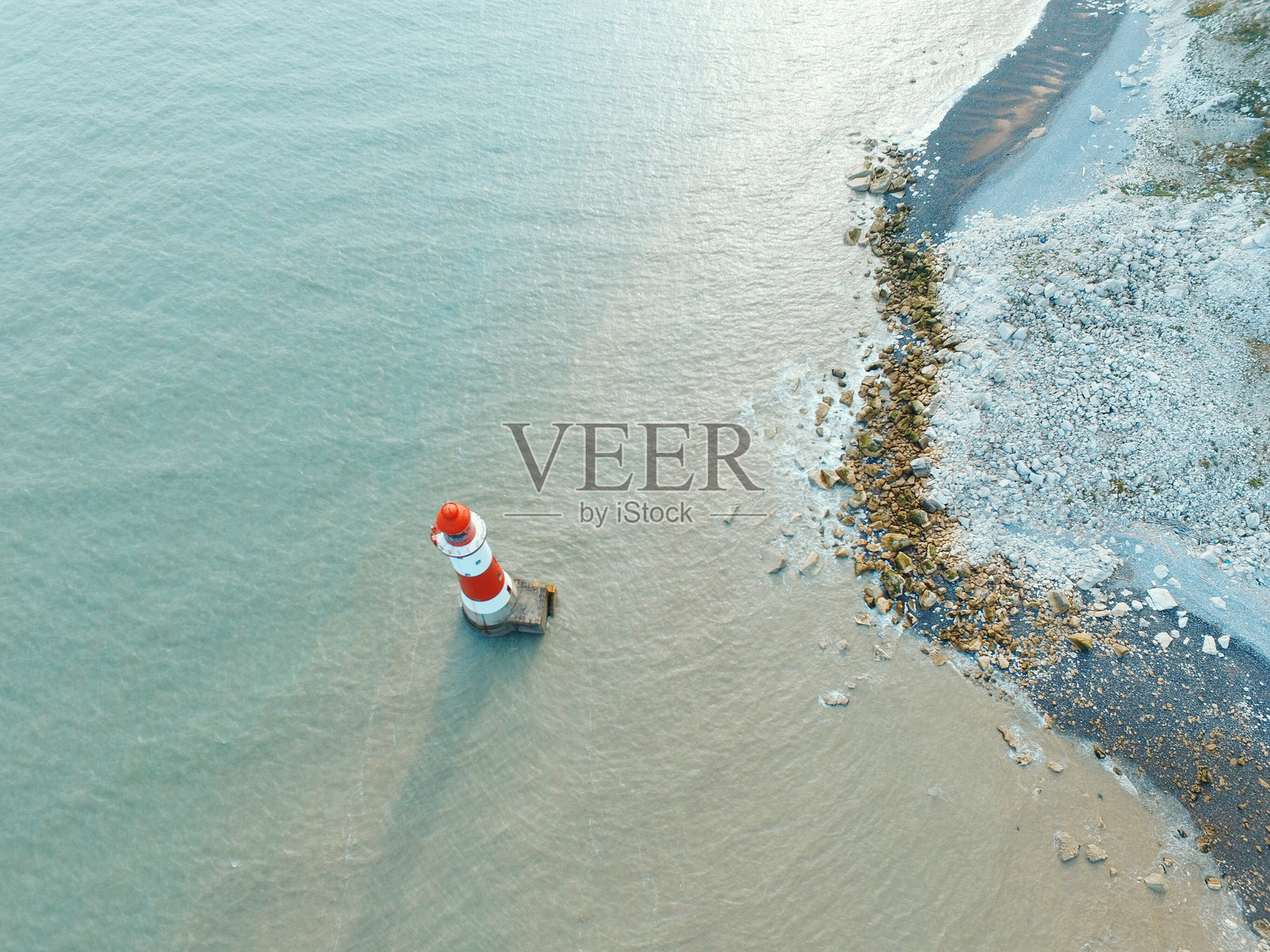 东堡的灯塔、平静的海洋和岩石海滩的鸟瞰图照片摄影图片