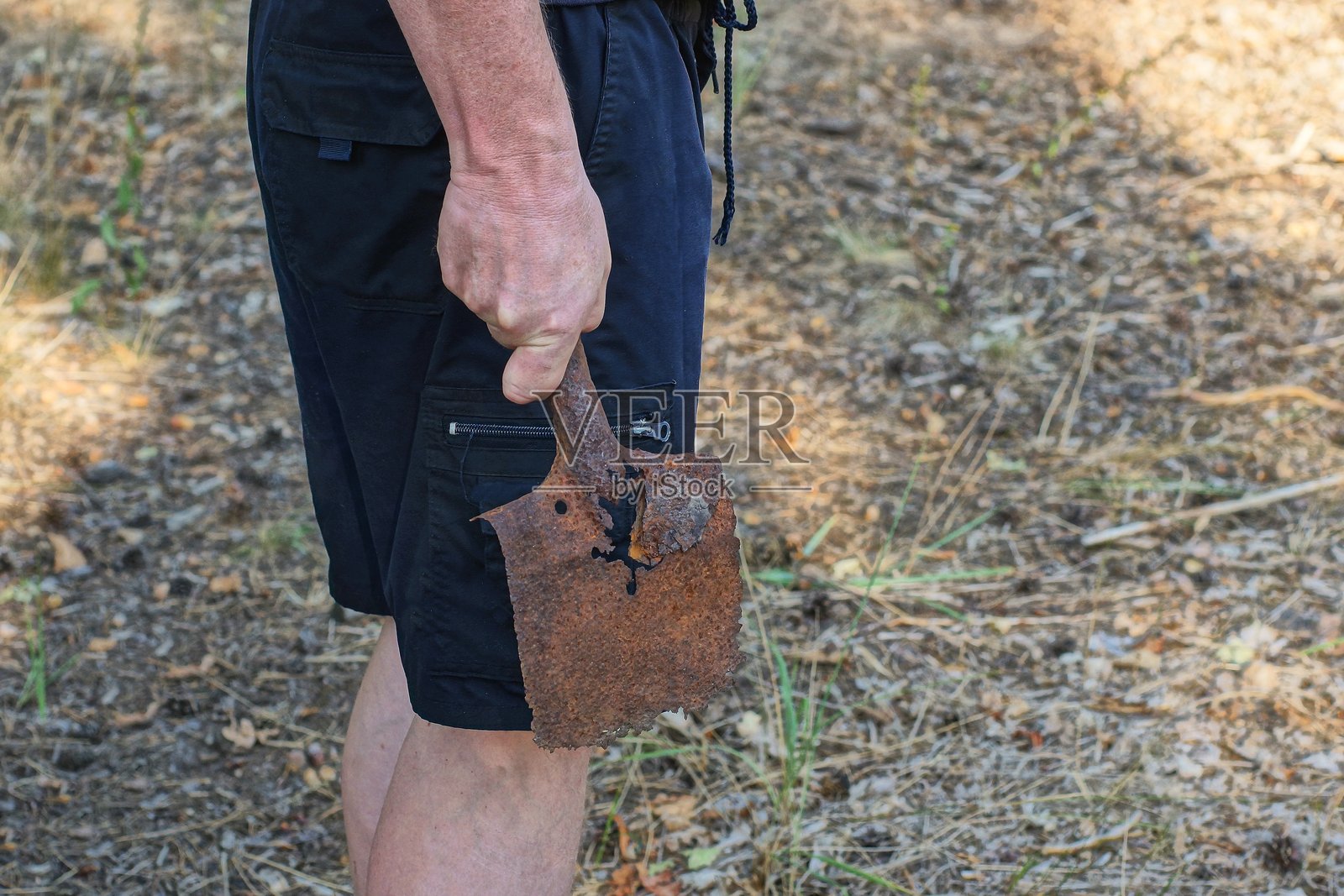 一只穿着蓝色衣服的男人的手握着一把旧的生锈棕色铁铲。照片摄影图片