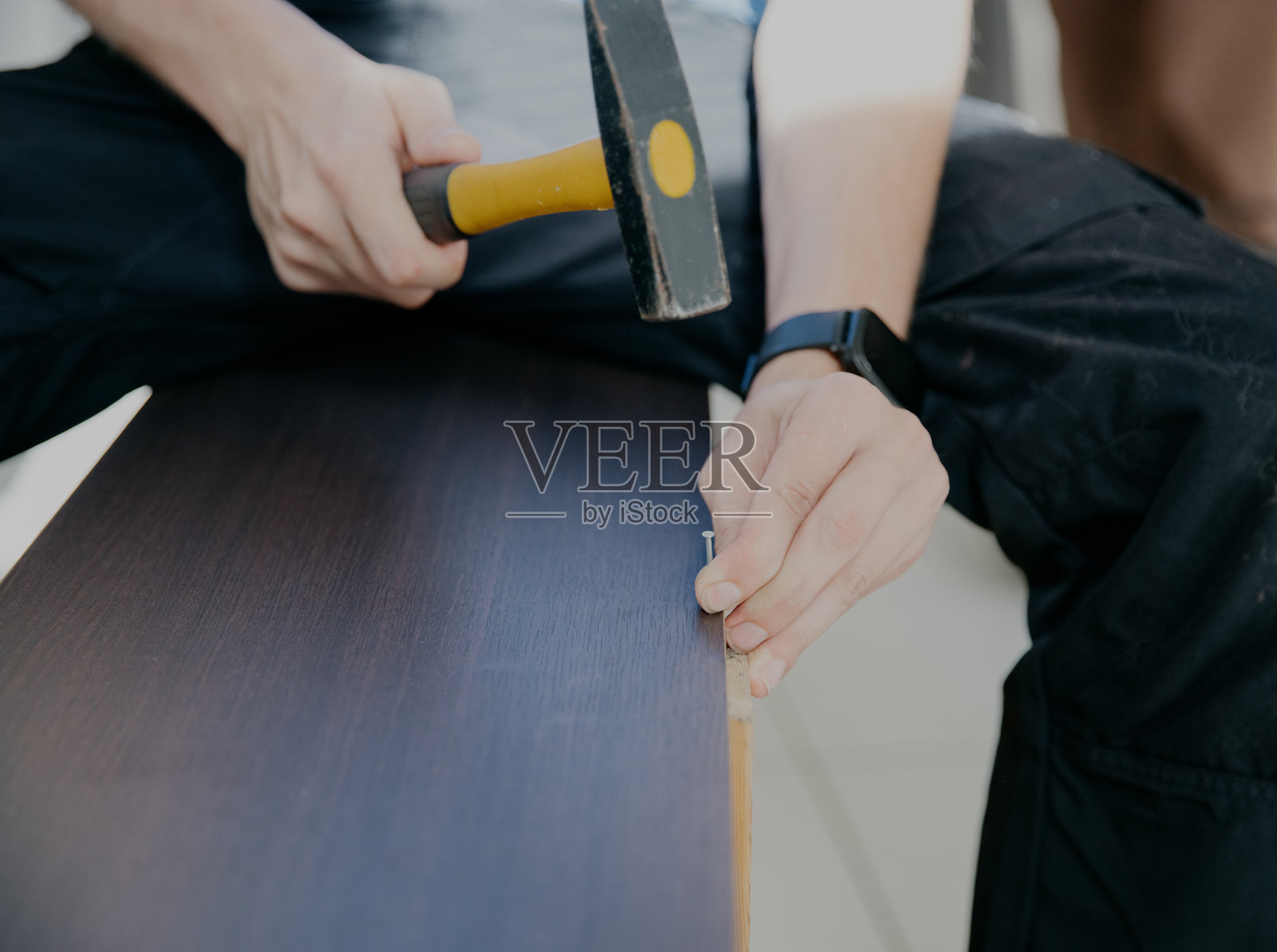 一个年轻人正在用锤子修理一个旧橱柜。照片摄影图片