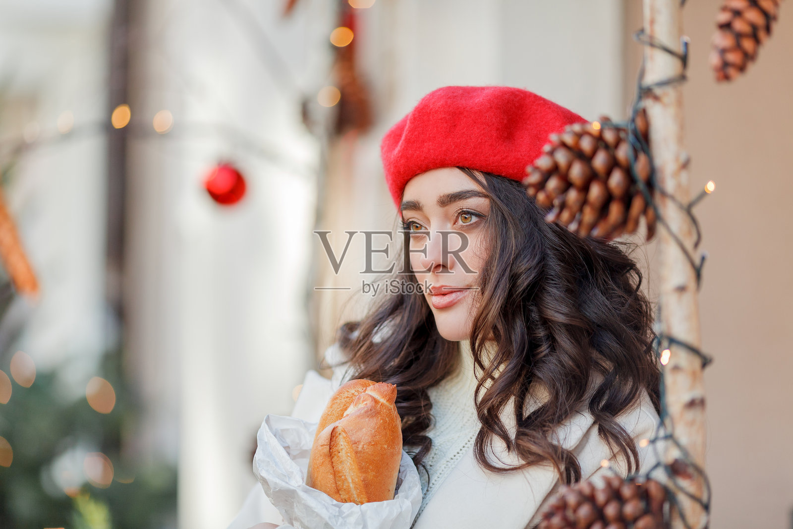 一位年轻美丽的女性在欧洲城市中，戴着红色贝雷帽。年轻女性手中拿着装有法棍的纸袋。圣诞节。照片摄影图片