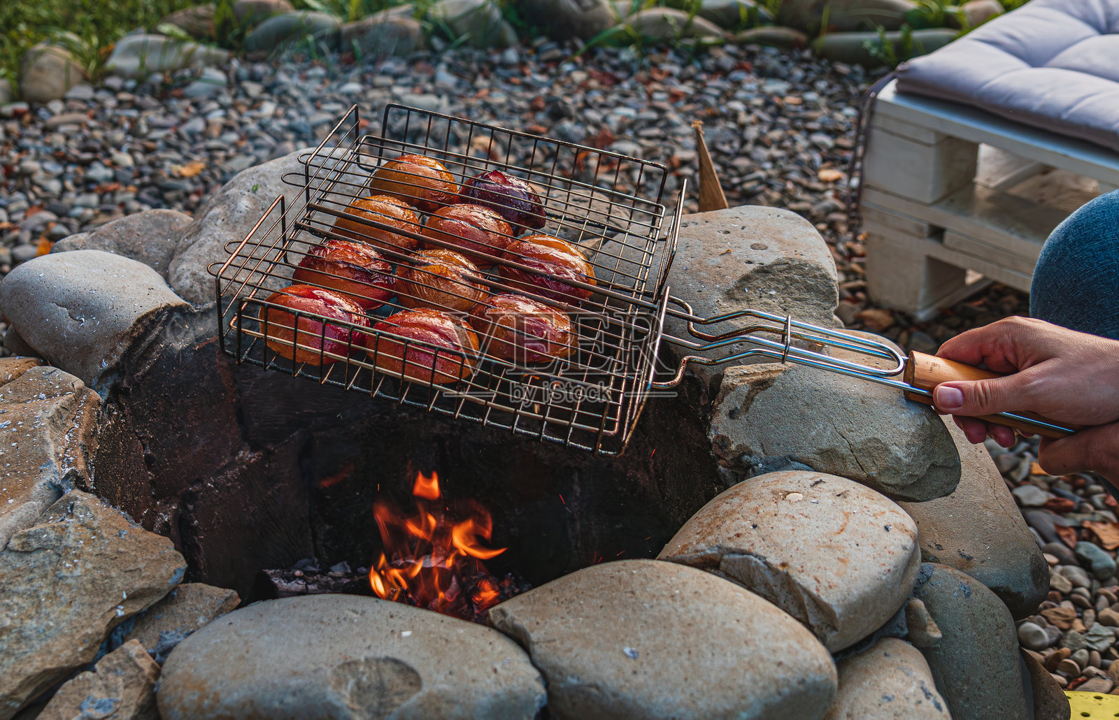 女性手中握着在明火上烤制的桃子，表面焦糖化的纹理在烤架上显现。照片摄影图片