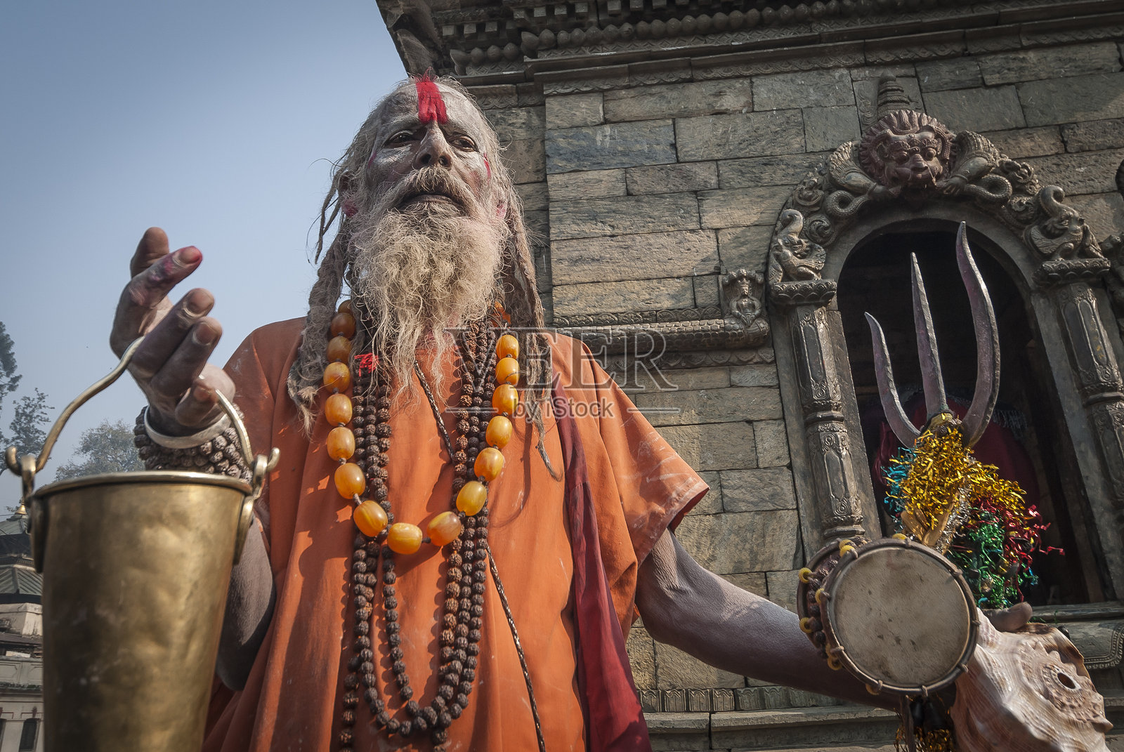 身穿藏红色袍子的圣者，帕斯帕提纳特寺，手持施舍桶和三叉戟，尼泊尔加德满都照片摄影图片