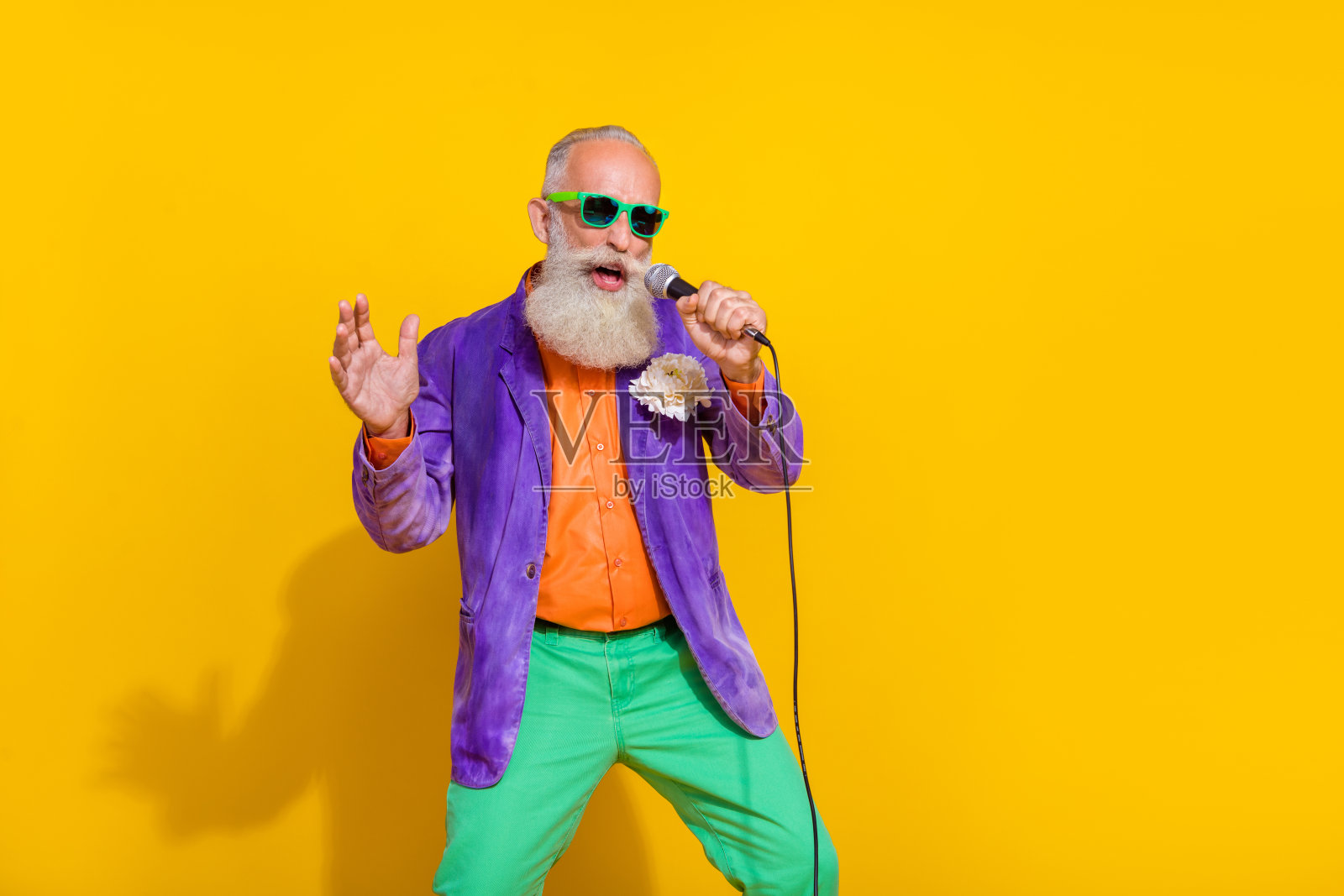 酷炫的嘻哈风退休男士摇滚歌手在鲜艳色彩背景下唱卡拉OK麦克风照片摄影图片