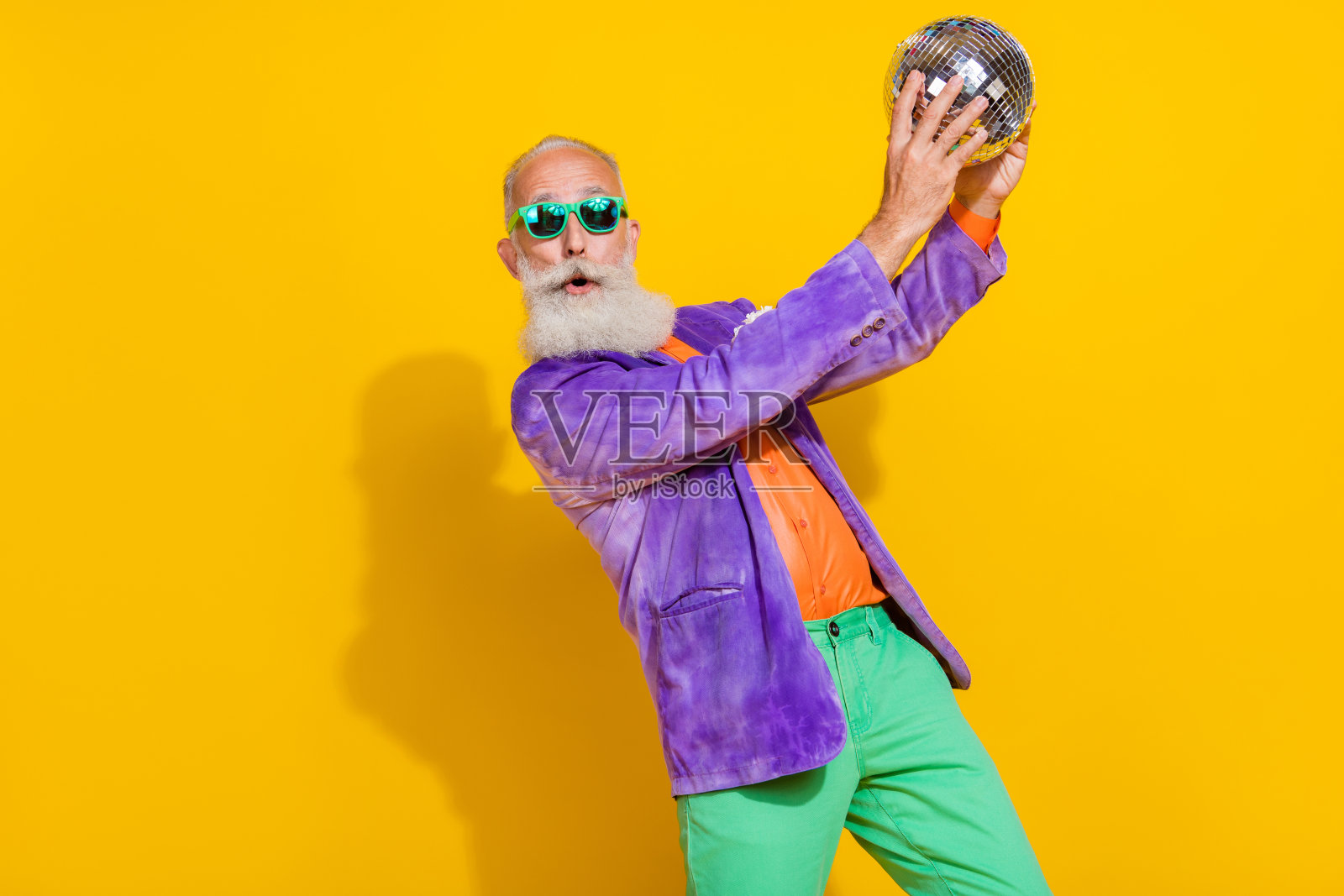 优雅整洁的老年人双手握着发光的迪斯科球，背景为黄色。照片摄影图片
