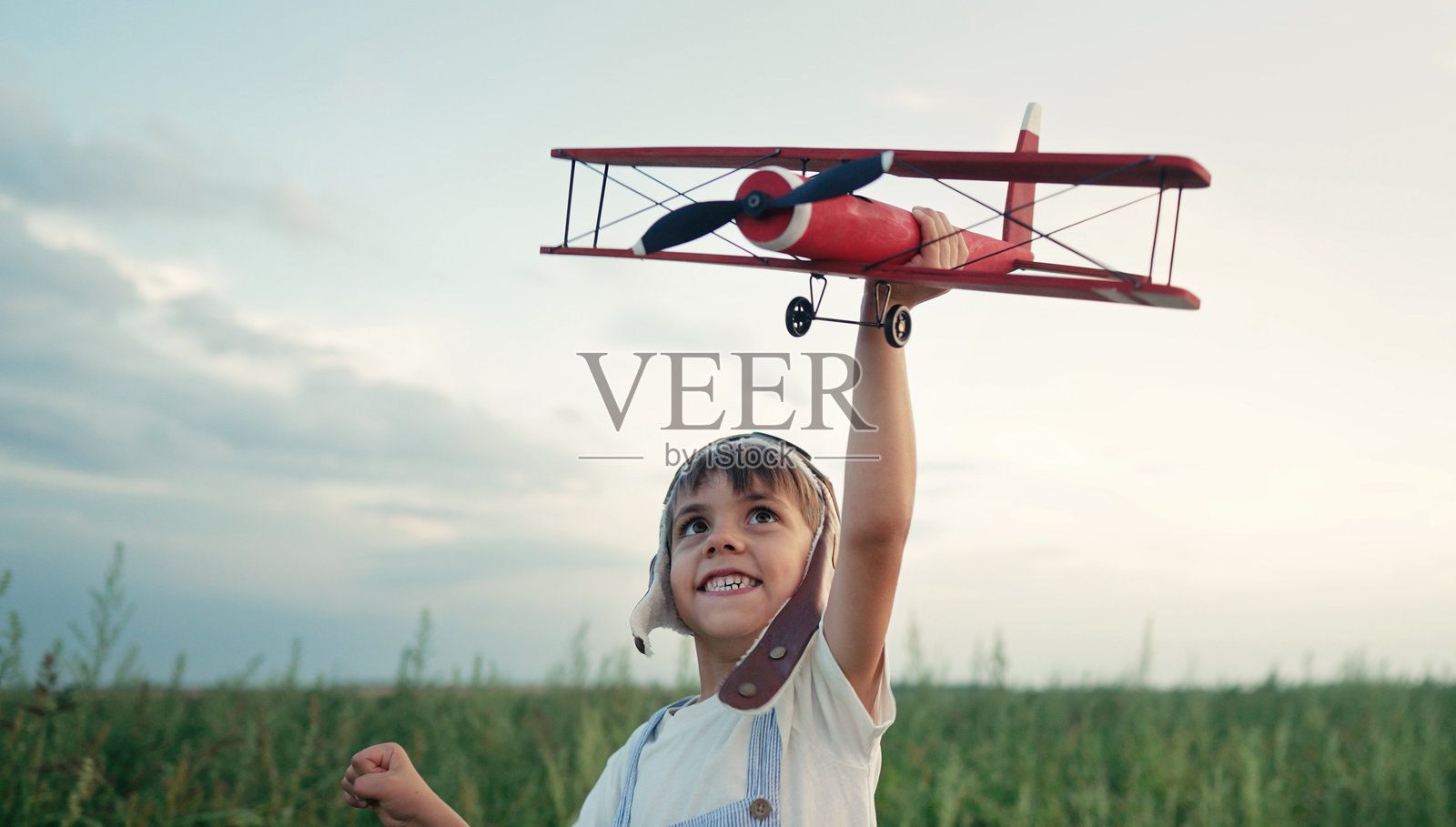 微笑着的5岁男孩对木制飞机感兴趣，探索未来职业的兴趣，梦想着在夏季田野上飞翔和旅行。创造性的梦想，幻想，童年。照片摄影图片