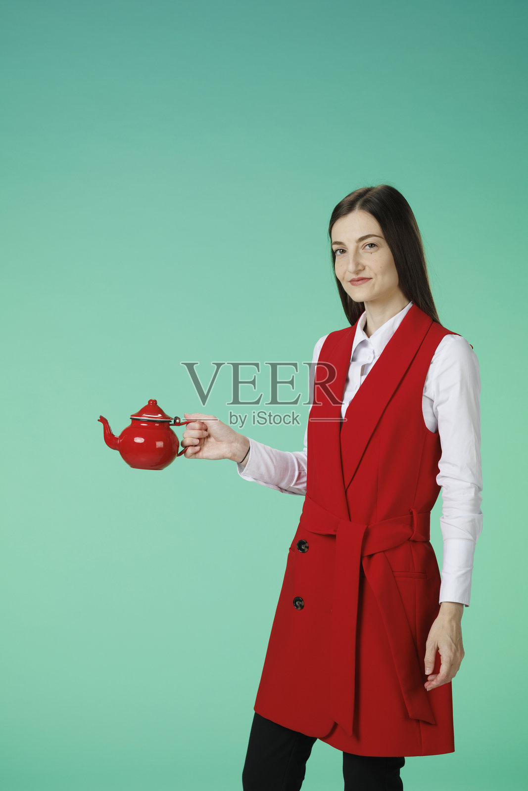 茶歇时光。动感肖像美丽的女商人，从红色茶壶中倒茶。红白优雅的生活方式。碧绿色背景。照片摄影图片