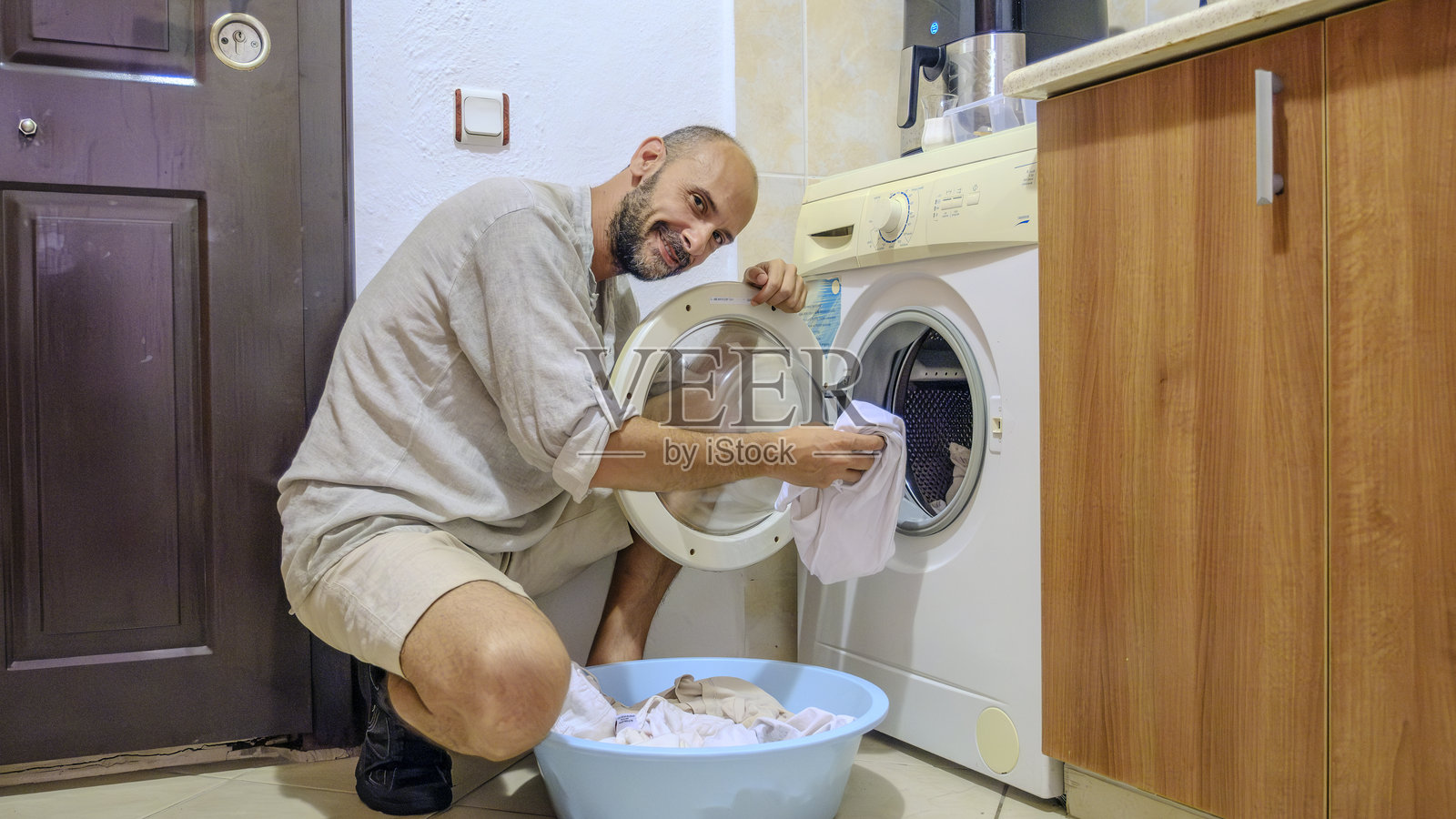 一个有魅力的中年男子在阳光明媚的夏日里在家做家务，把白色脏衣服放进洗衣机里。照片摄影图片
