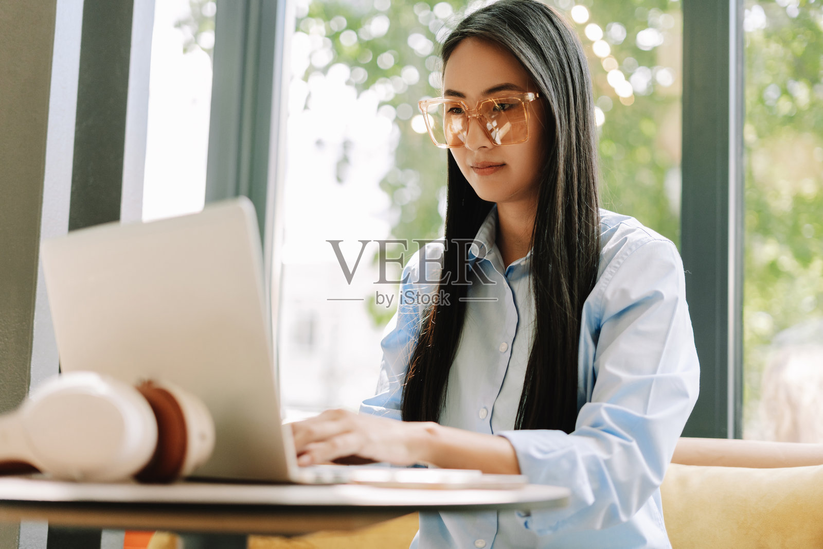 年轻的亚洲女性戴着时尚眼镜，在咖啡馆里使用笔记本电脑工作照片摄影图片