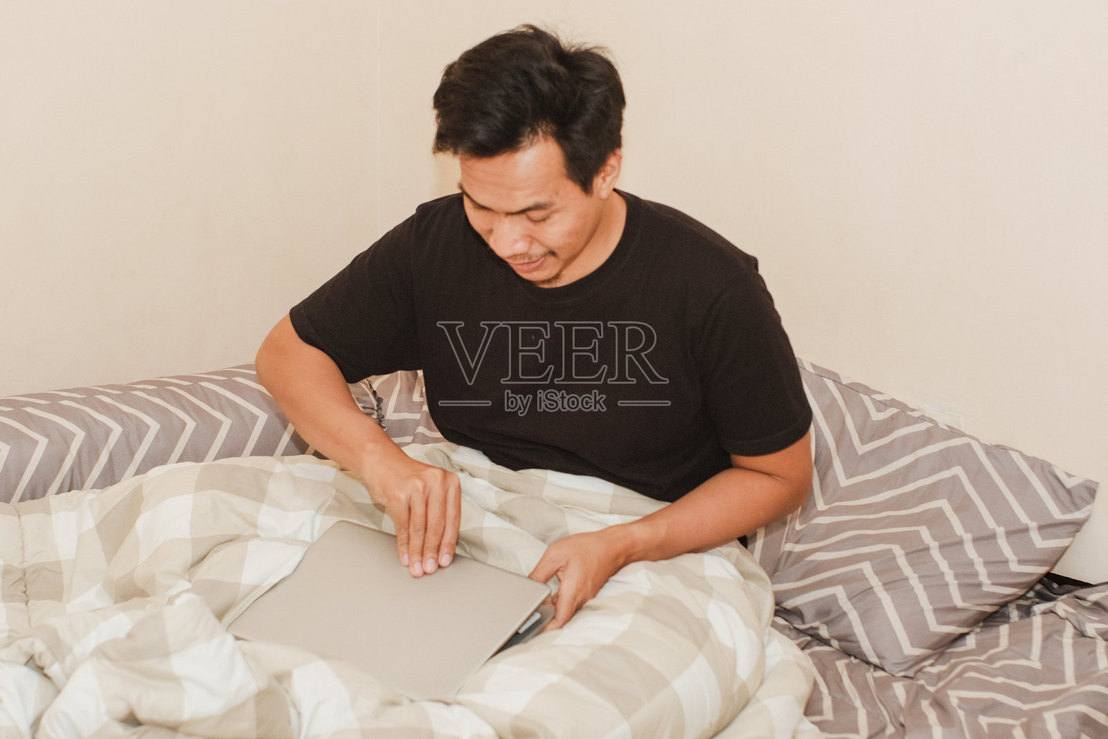 一位东南亚男子在早晨床上打开笔记本电脑准备工作照片摄影图片