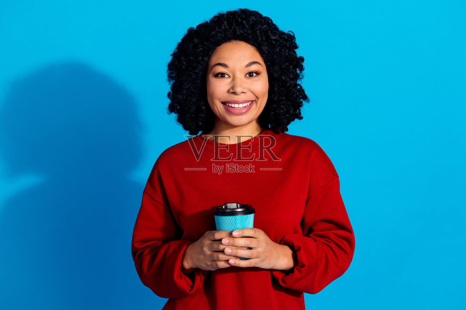 可爱的年轻女士手持纸杯咖啡，穿着时尚的红色服装，背景为蓝色。照片摄影图片