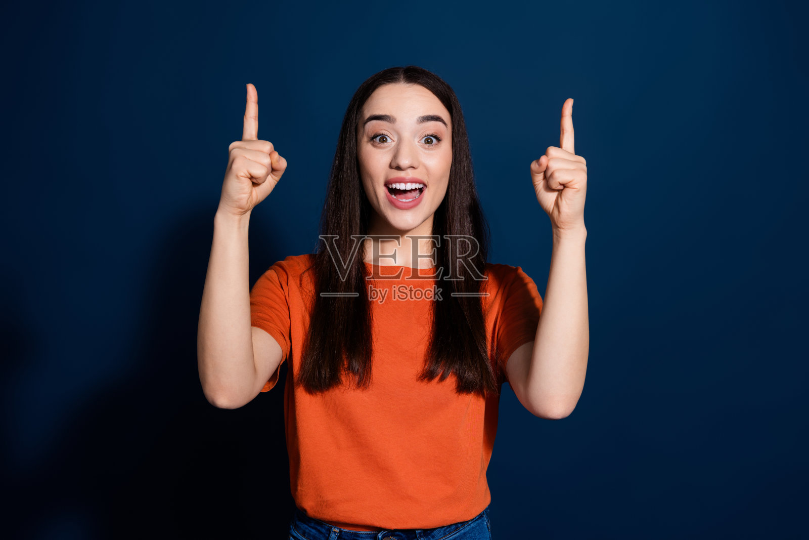 迷人积极的女性穿着橙色时尚服装，推荐海报空白区域，背景为深蓝色。照片摄影图片