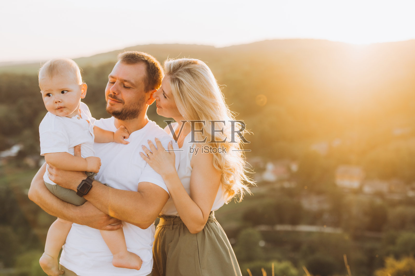 在黄金时刻的自然中，幸福的家庭时刻，父母在户外拥抱宝宝的肖像照片摄影图片