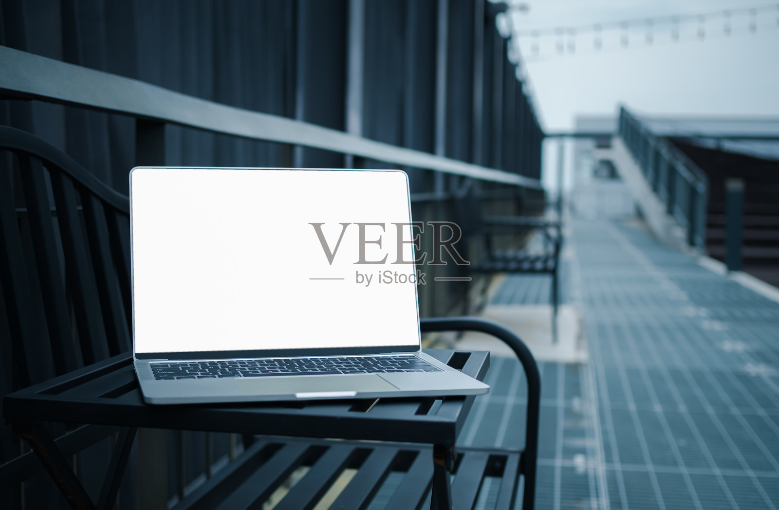 一台白色空白屏幕的笔记本电脑放在现代城市走廊旁的金属桌子上，空白的复制空间，模糊背景中的笔记本电脑，学习和办公工作的概念。照片摄影图片