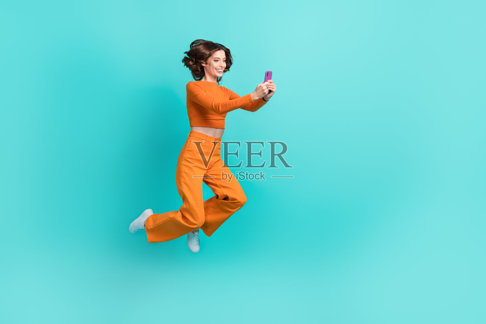 全身照的快乐女士，沉迷于手机，正在输入评论和转发，背景为青色，留有空白空间。照片摄影图片