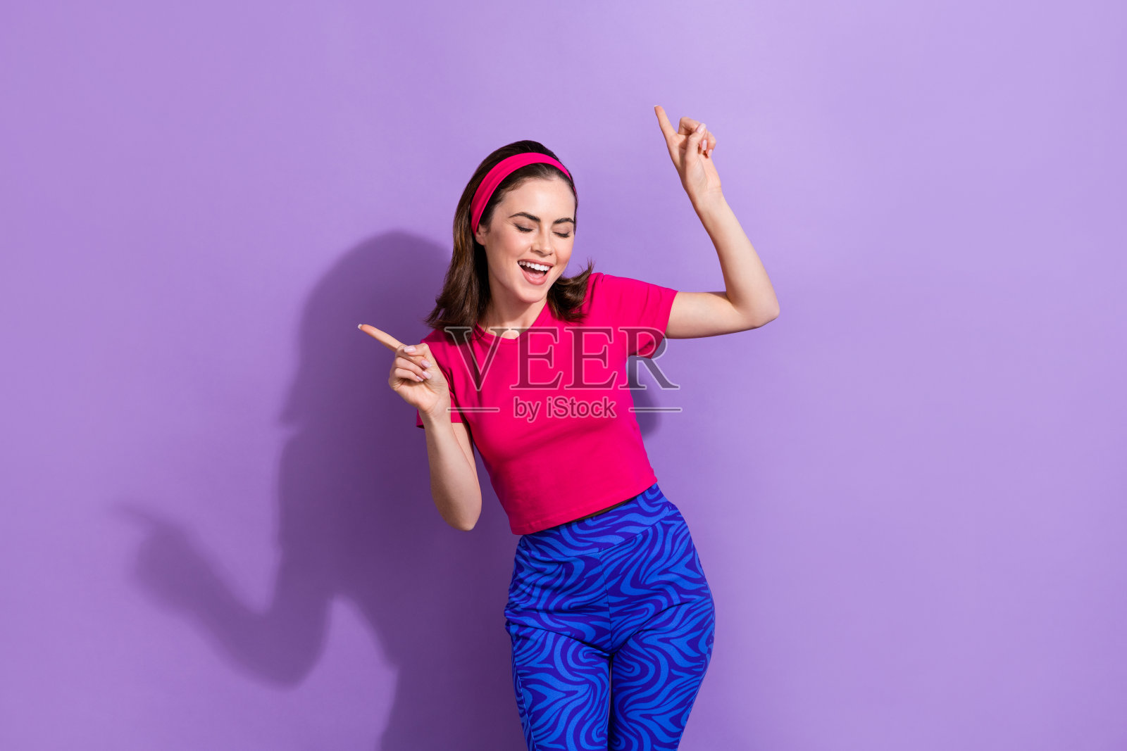 快乐的女士在紫色背景下指着自己，享受夜店舞蹈的乐趣。照片摄影图片
