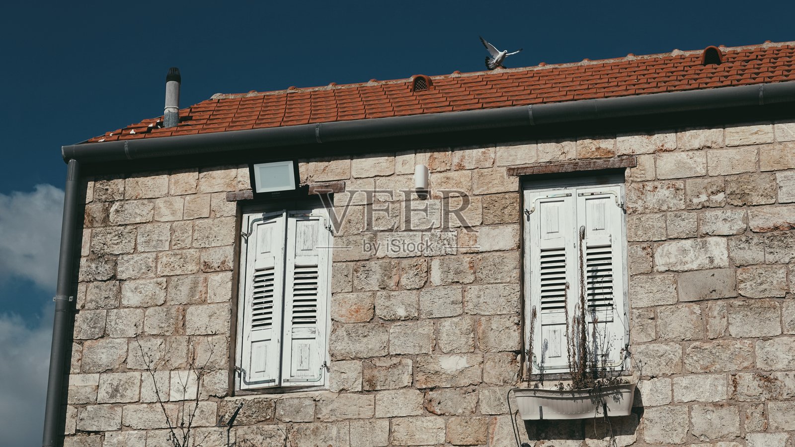 蓝天下带白色百叶窗的复古石头房子照片摄影图片
