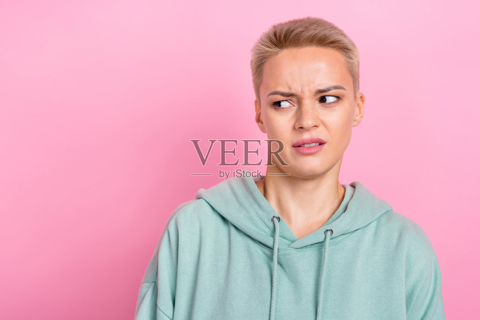 穿着时尚卡其色衣服的漂亮年轻女孩，面露厌恶和困惑的表情，背景为粉色，空旷无物。照片摄影图片