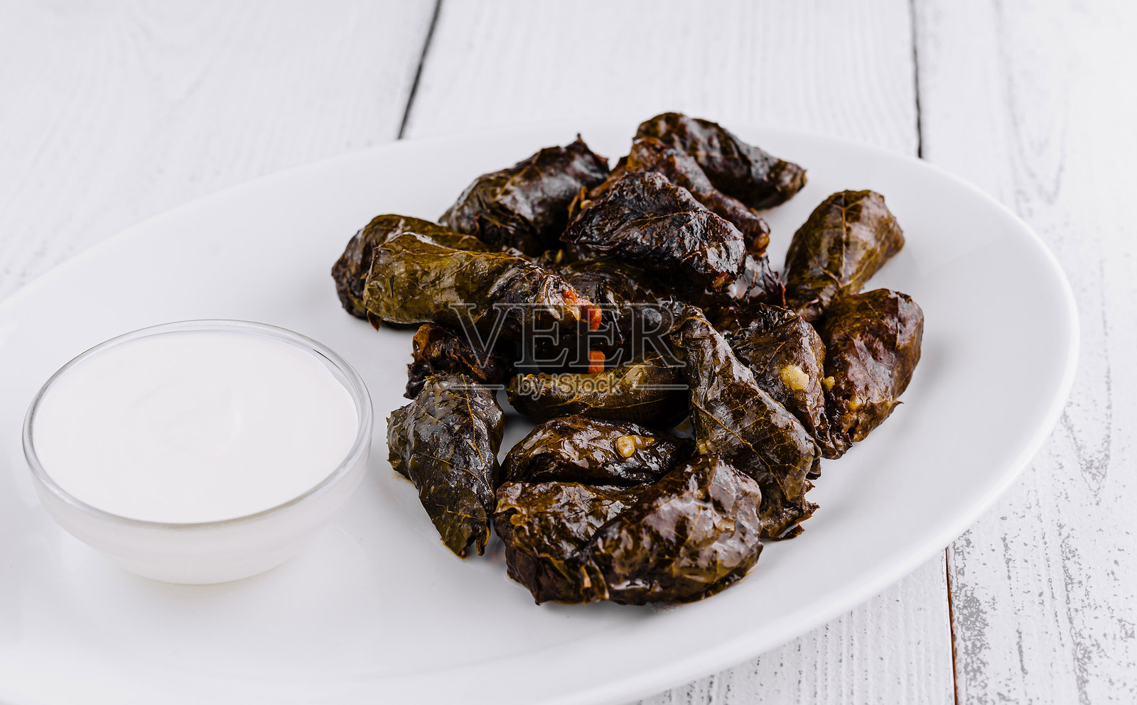 在乡村风格的白色桌子上，盛放着填充葡萄叶的多尔玛和酸奶酱的餐盘照片摄影图片