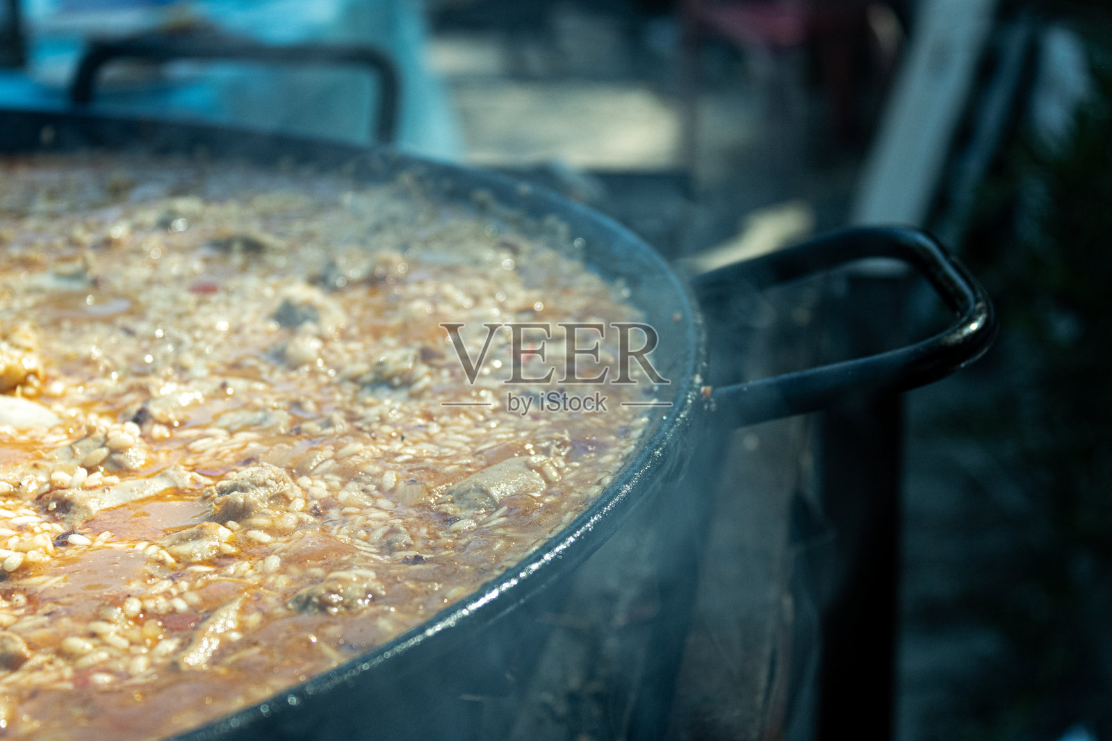 在街头美食节上，火上煮着一大锅西班牙海鲜饭，背景烟雾缭绕。照片摄影图片