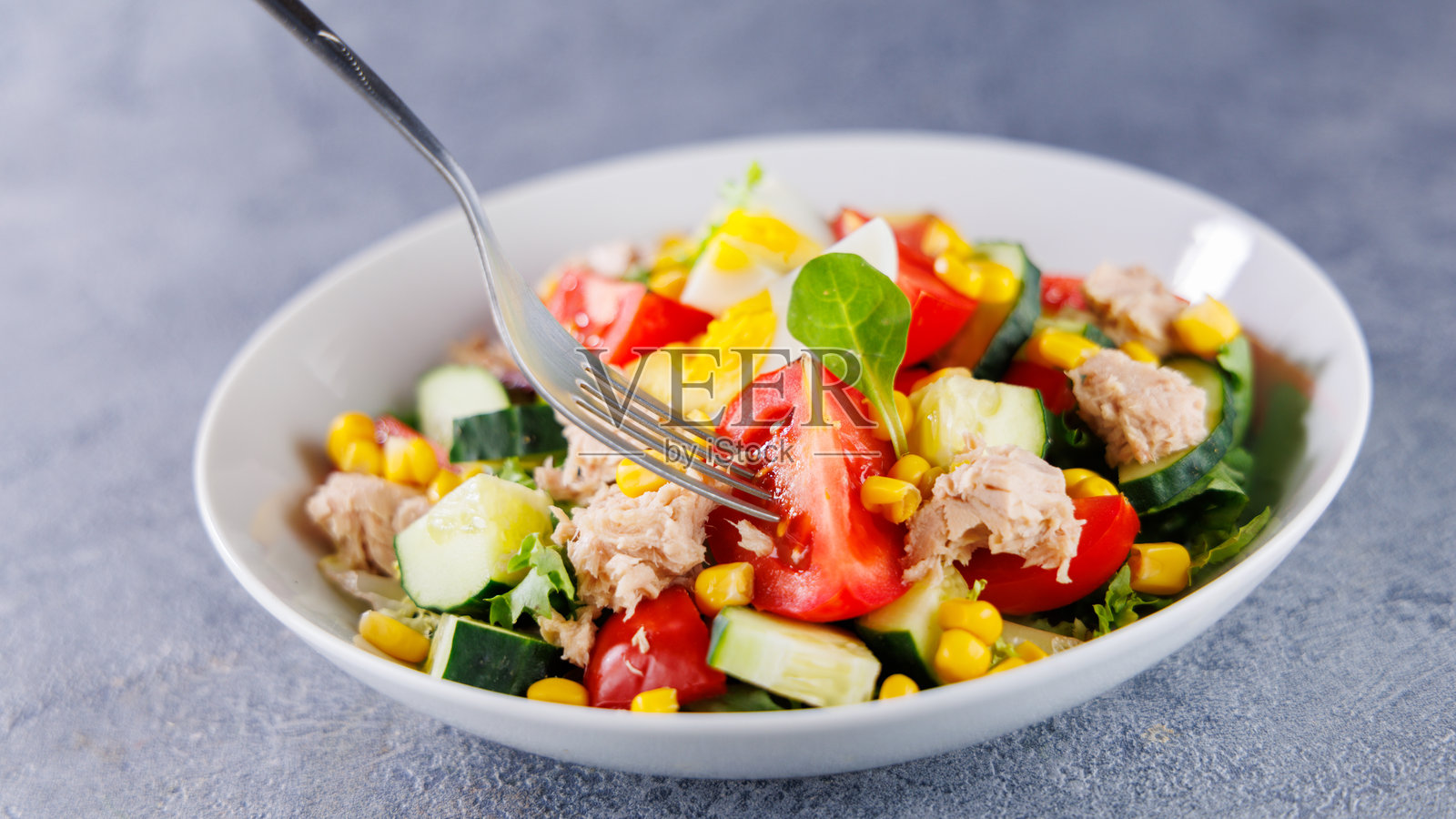 混合沙拉，配有鸡蛋、西红柿、玉米、黄瓜和金枪鱼，健康餐搭配叉子照片摄影图片