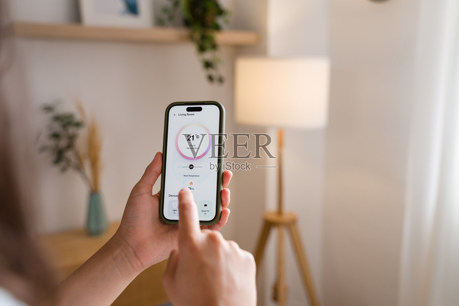 女人用智能手机上的智能家居应用程序控制家里的温度照片摄影图片